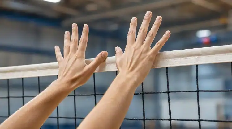 Close-up of a volleyball blocker's hands reaching over the net with fingers spread